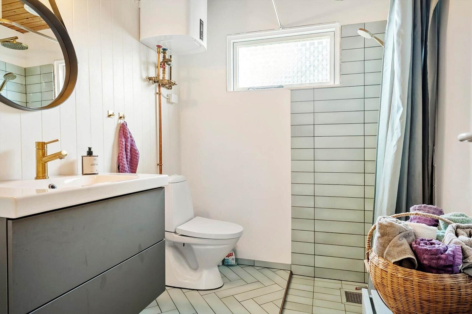 Badezimmer mit Waschbecken, Toilette und Dusche mit Bademattenkorb.