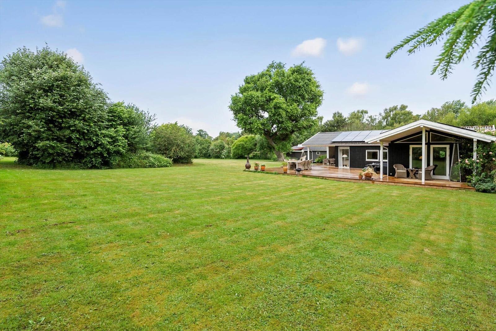 Haus mit Terrasse und großem Garten unter Bäumen.