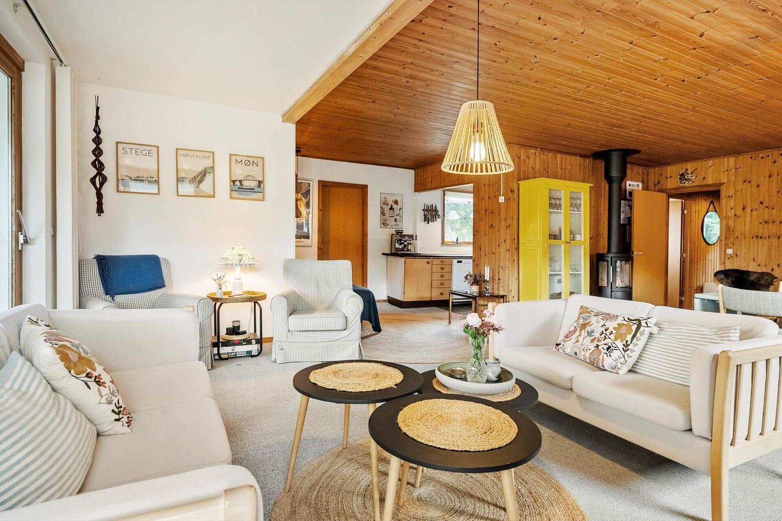 Wohnzimmer mit Sofa, Sesseln und Holzdecke. Gelber Schrank und Kamin sichtbar.