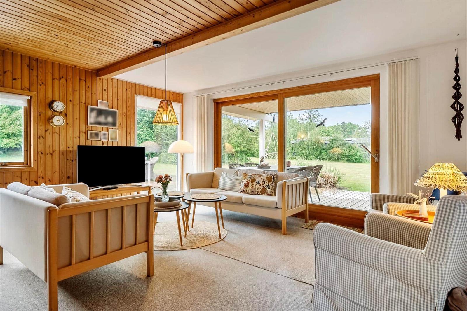 Wohnzimmer mit Holzwand, Sofa, Fernseher und Blick auf die Terrasse.