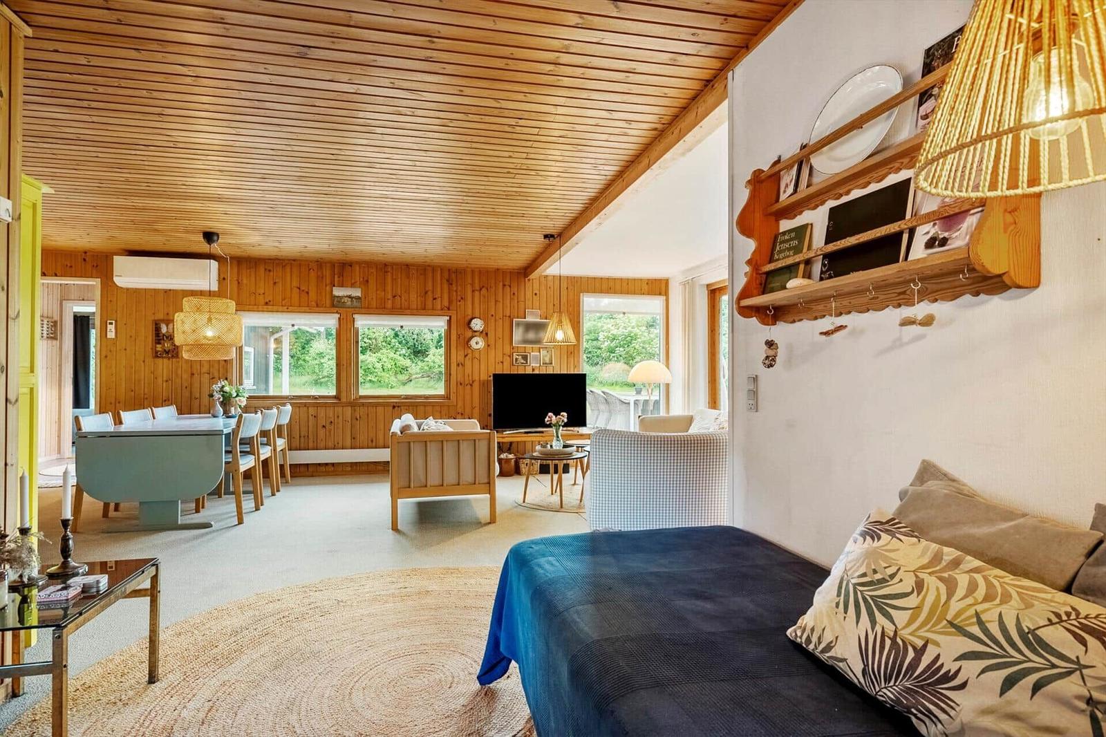 Wohn- und Essbereich mit Holzdecke, Sofa, Tisch und Fenstern.