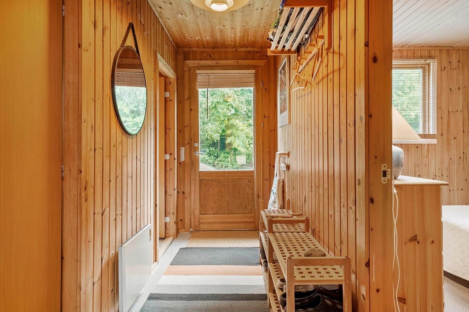 Holzgetäfelte Flur mit Spiegel, Schuhschrank und Tür zum Garten.