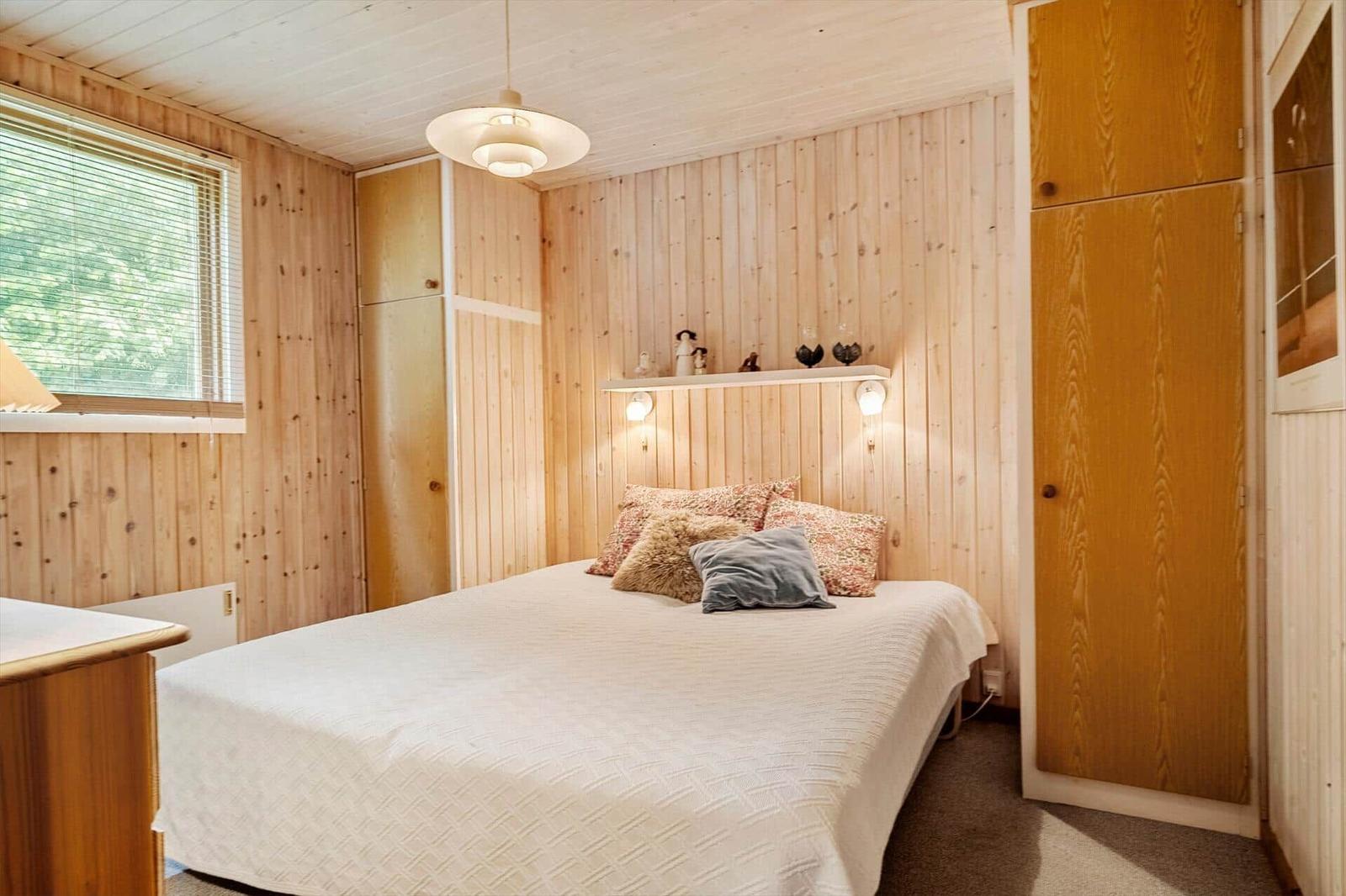 Schlafzimmer mit Holzwand, Bett, Kleiderschrank und Fenster mit Jalousie.