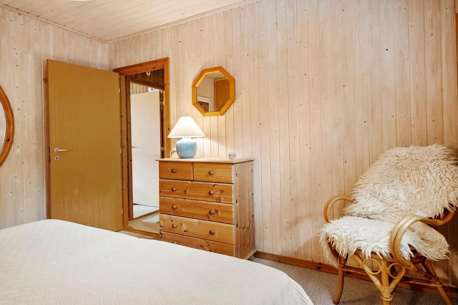 Schlafzimmer mit Holzwand, Bett, Schrank, Stuhl und Spiegel.
