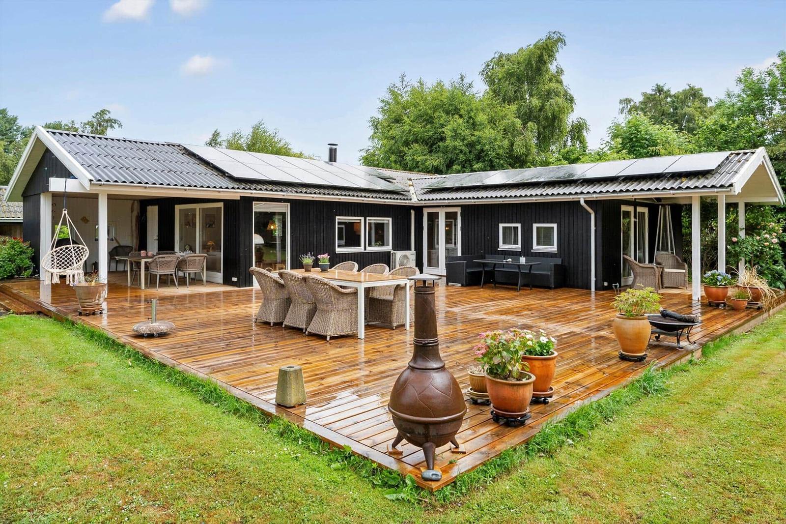 Schwarze Holzhütte mit großem Holzterrasse, Gartenmöbeln und Pflanzen.