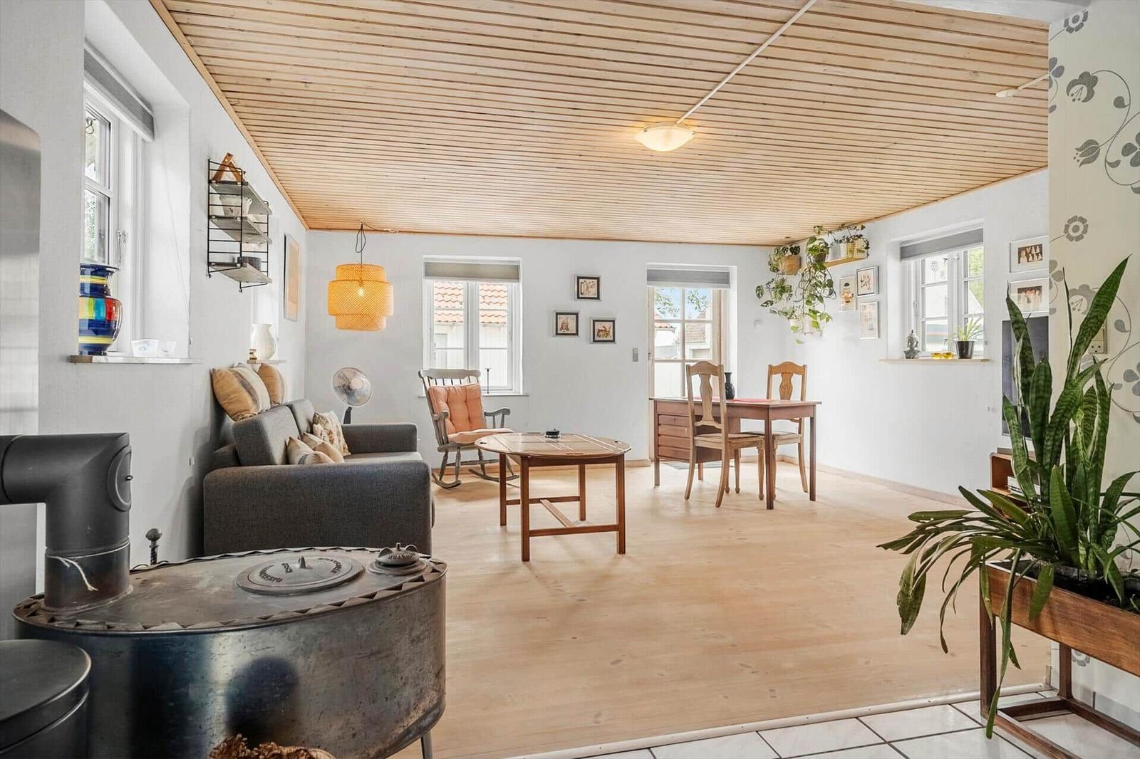 Wohn- und Essbereich mit Holzboden, Decke und Möbeln. Zimmer mit Fenstern und Pflanzen.