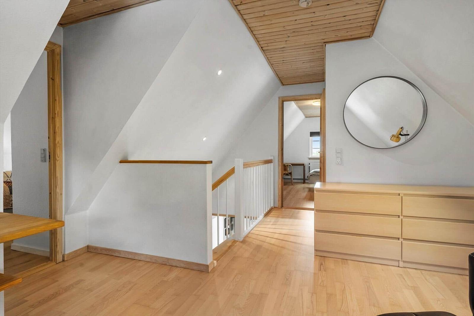 Dachgeschoss mit Holzboden, Treppe und Schrank. Runde Spiegel an der Wand.