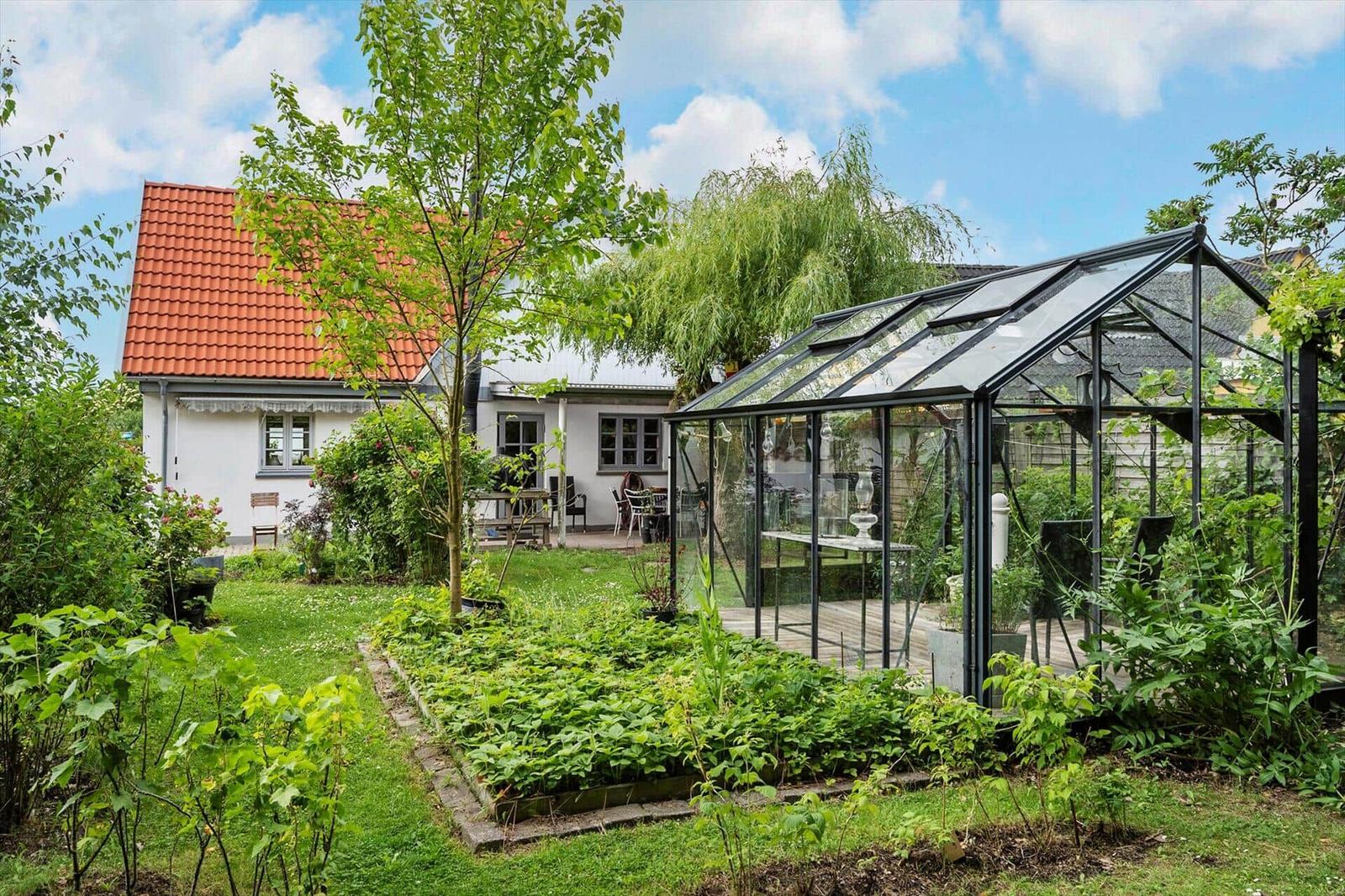 Haus mit Garten, Gewächshaus und Terrasse unter blauem Himmel.