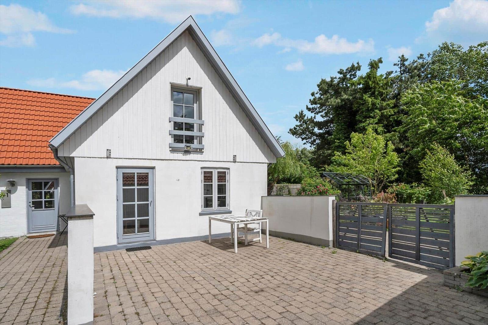 Wohnhaus mit Terrasse, Tisch und Stühlen, umgeben von Grünflächen und einem Zaun.