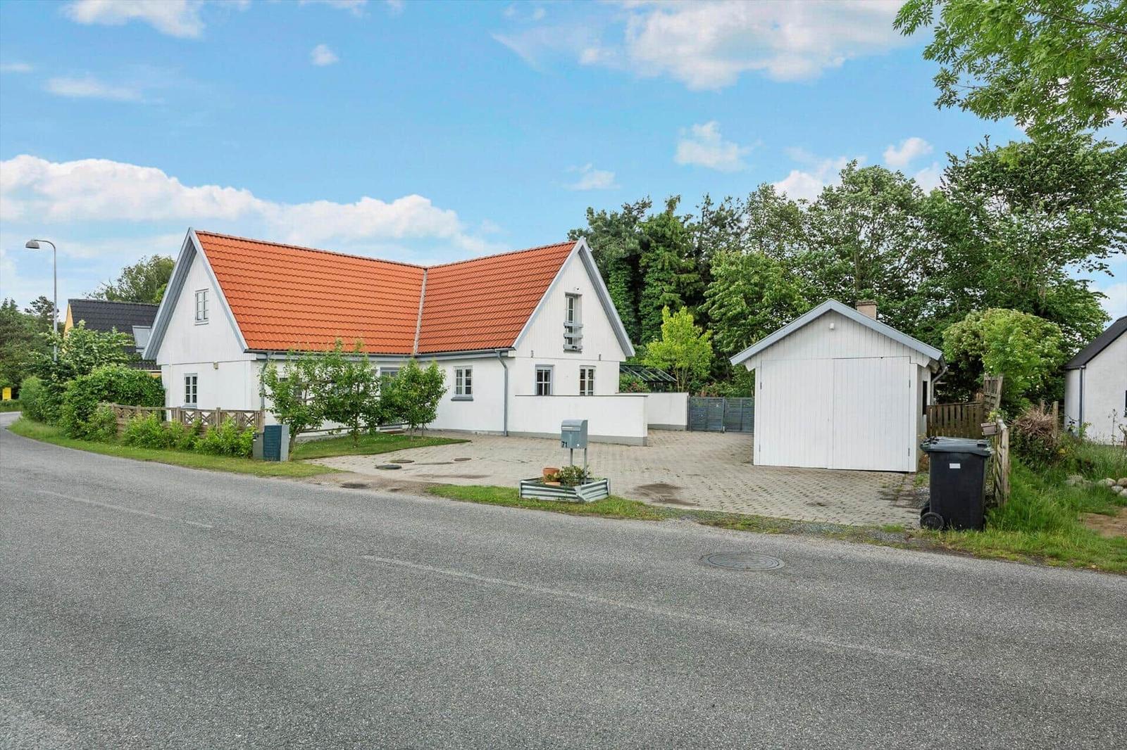 Weiße Villa mit rotem Dach, Garage und Gartenbereich an Straße.
