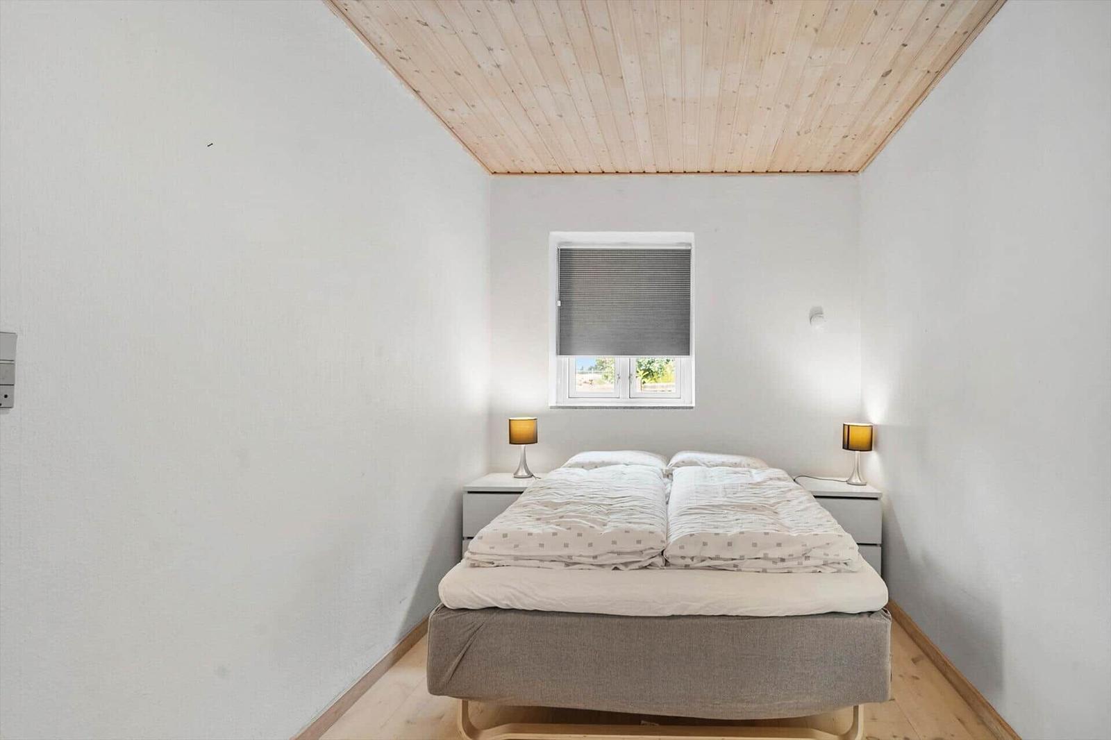 Schlafzimmer mit Doppelbett, zwei Nachttischen und einem Fenster mit Jalousie.