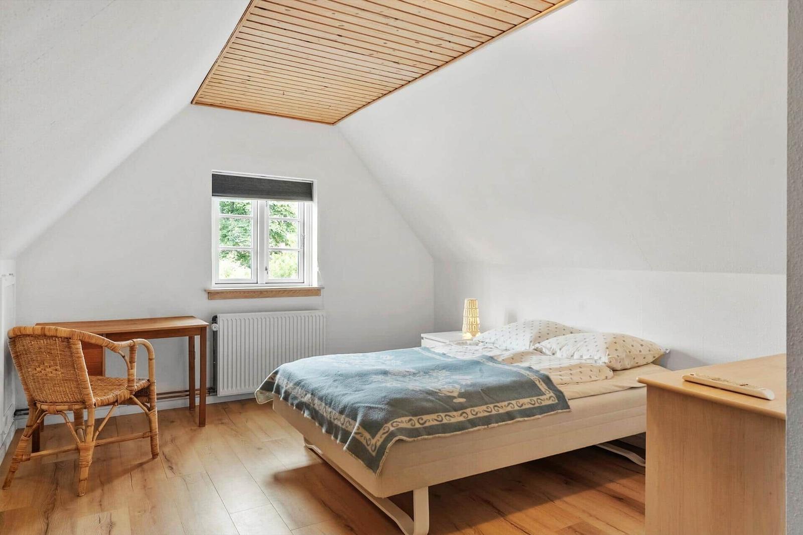 Schlafzimmer mit Dachschräge, Bett, Schreibtisch und Stuhl.