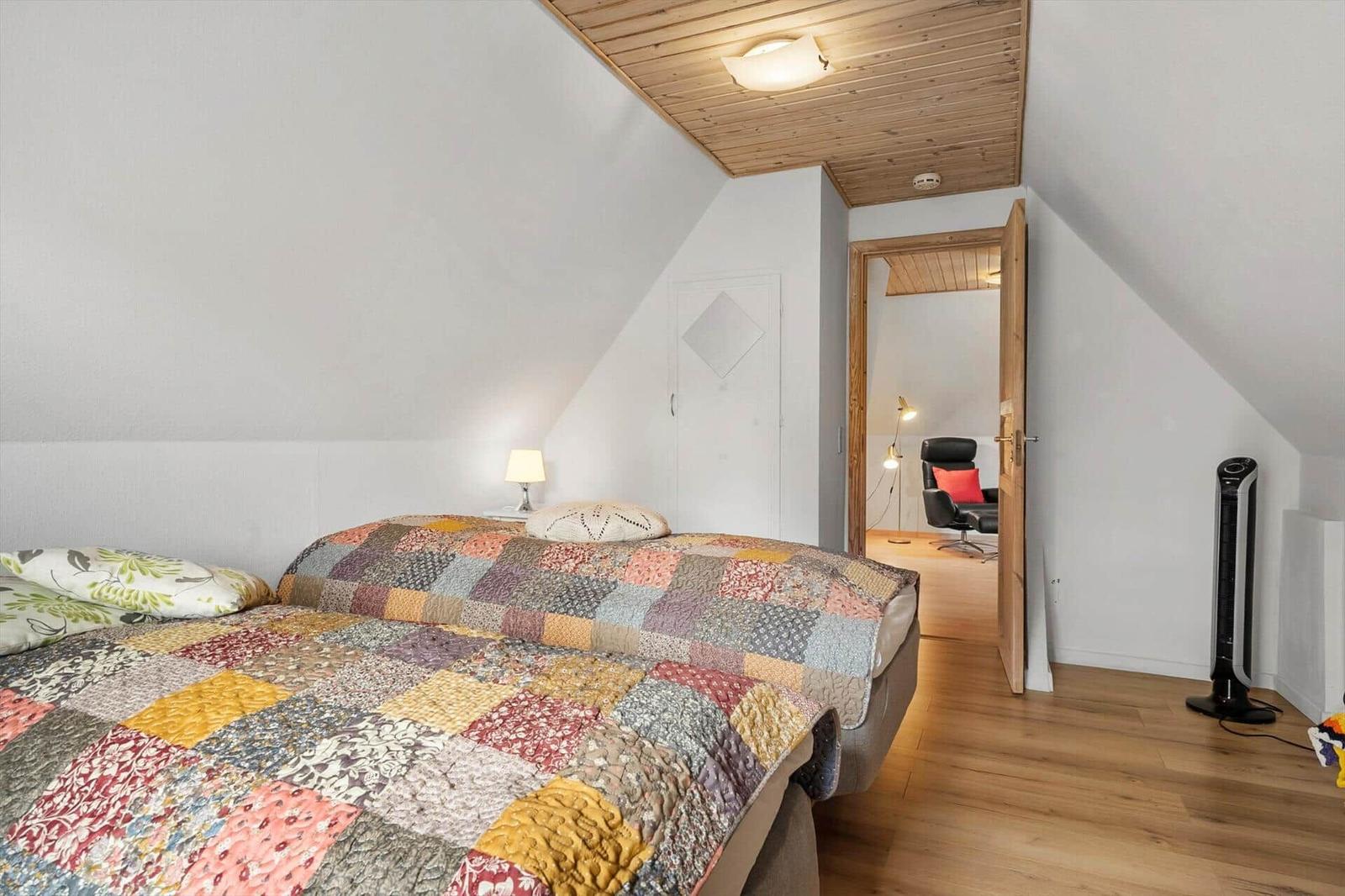 Schlafzimmer mit Bett, Holzdecke und Tür zum angrenzenden Raum.