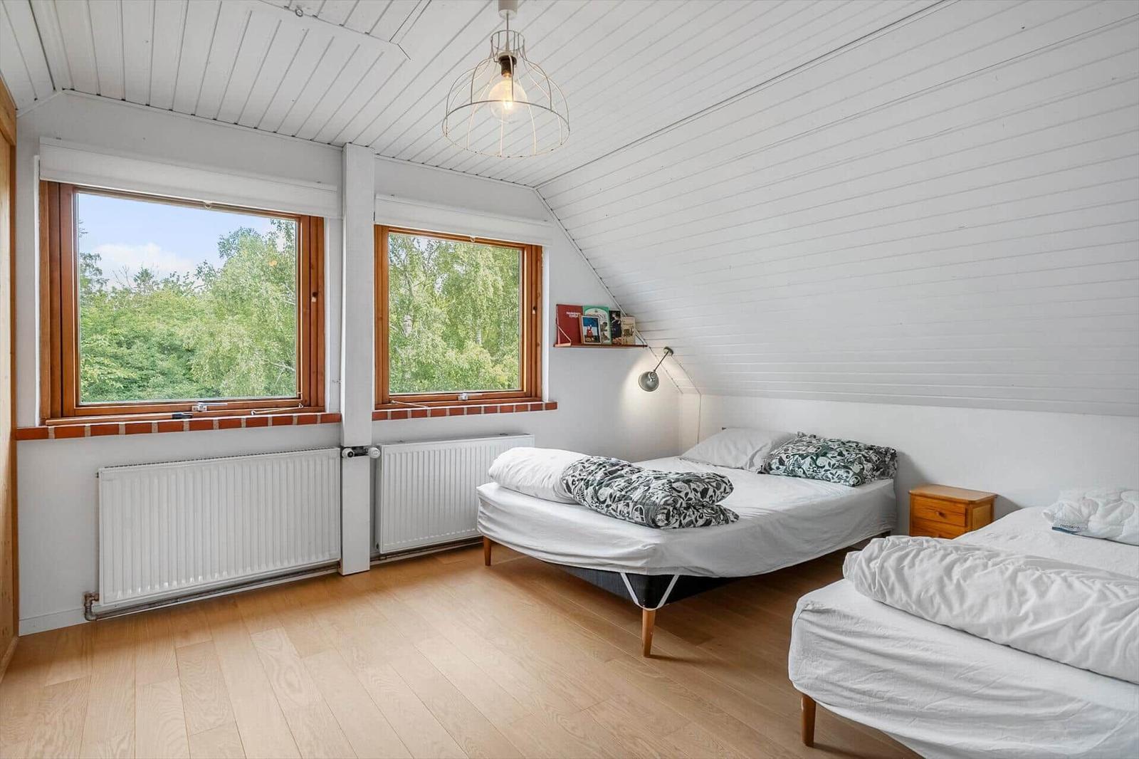 Zwei Betten, Fenster mit Blick auf Bäume, Holzboden, weiße Wände und Decke.