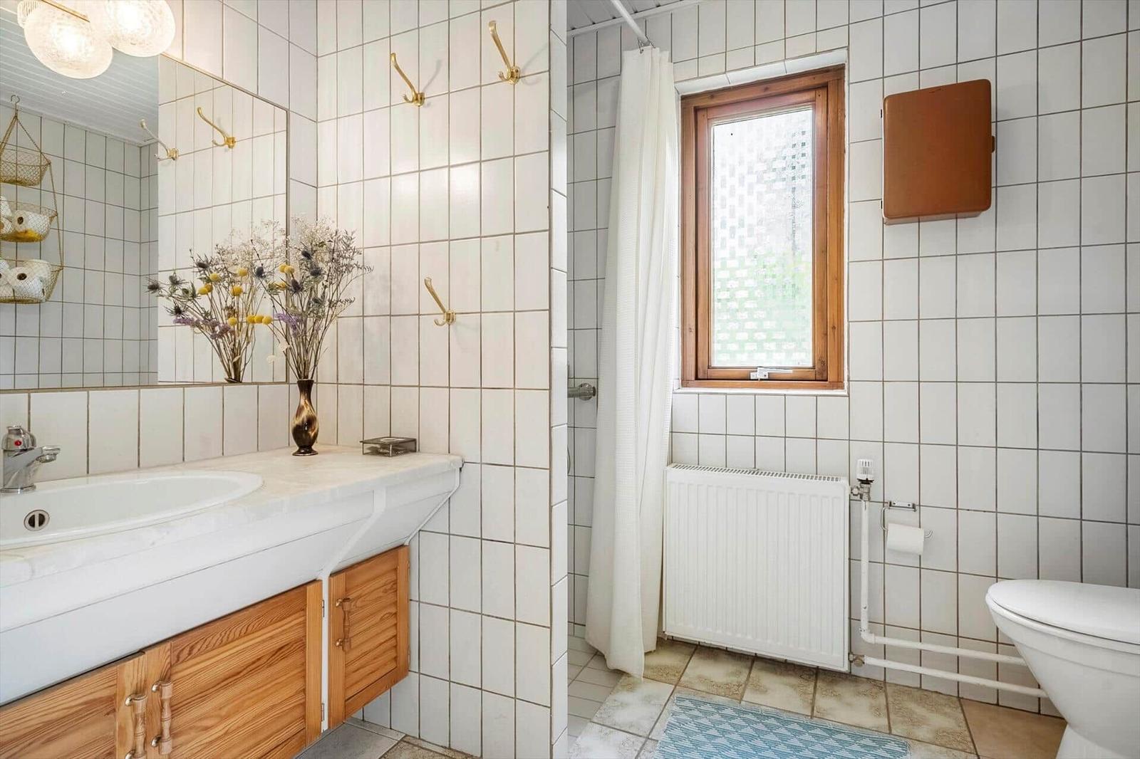Badezimmer mit Waschbecken, Dusche, Toilette und Fenster.