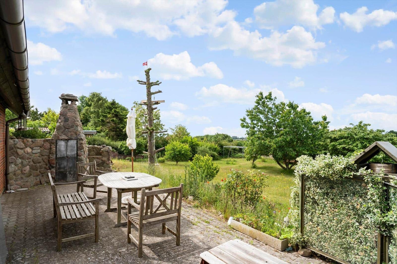 Terrasse mit Holztisch und Stühlen, Blick auf Garten und Baum mit Flagge.
