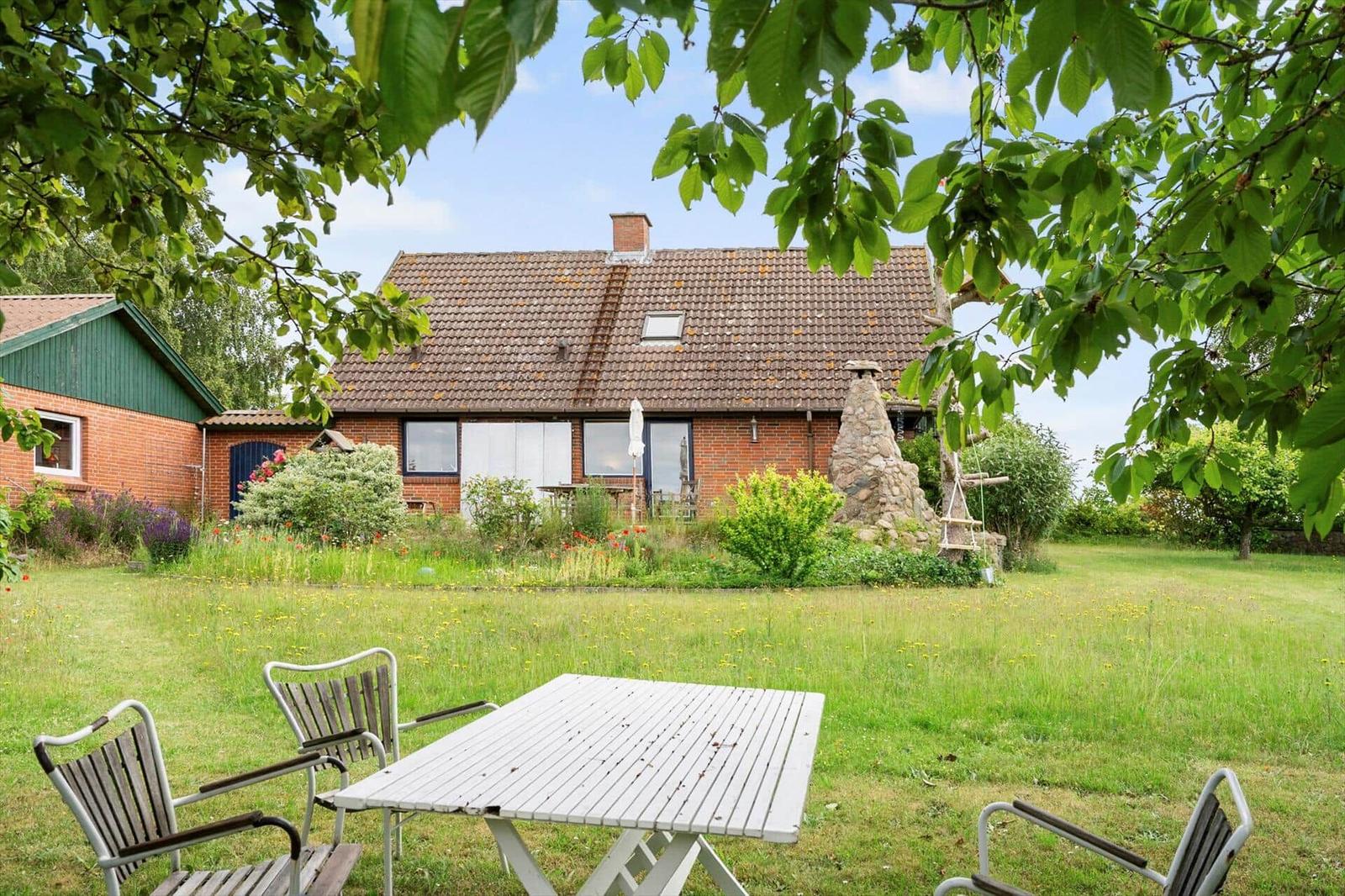 Haus mit Garten, Terrasse und Grillplatz. Blick durch Baumkronen auf das Anwesen.