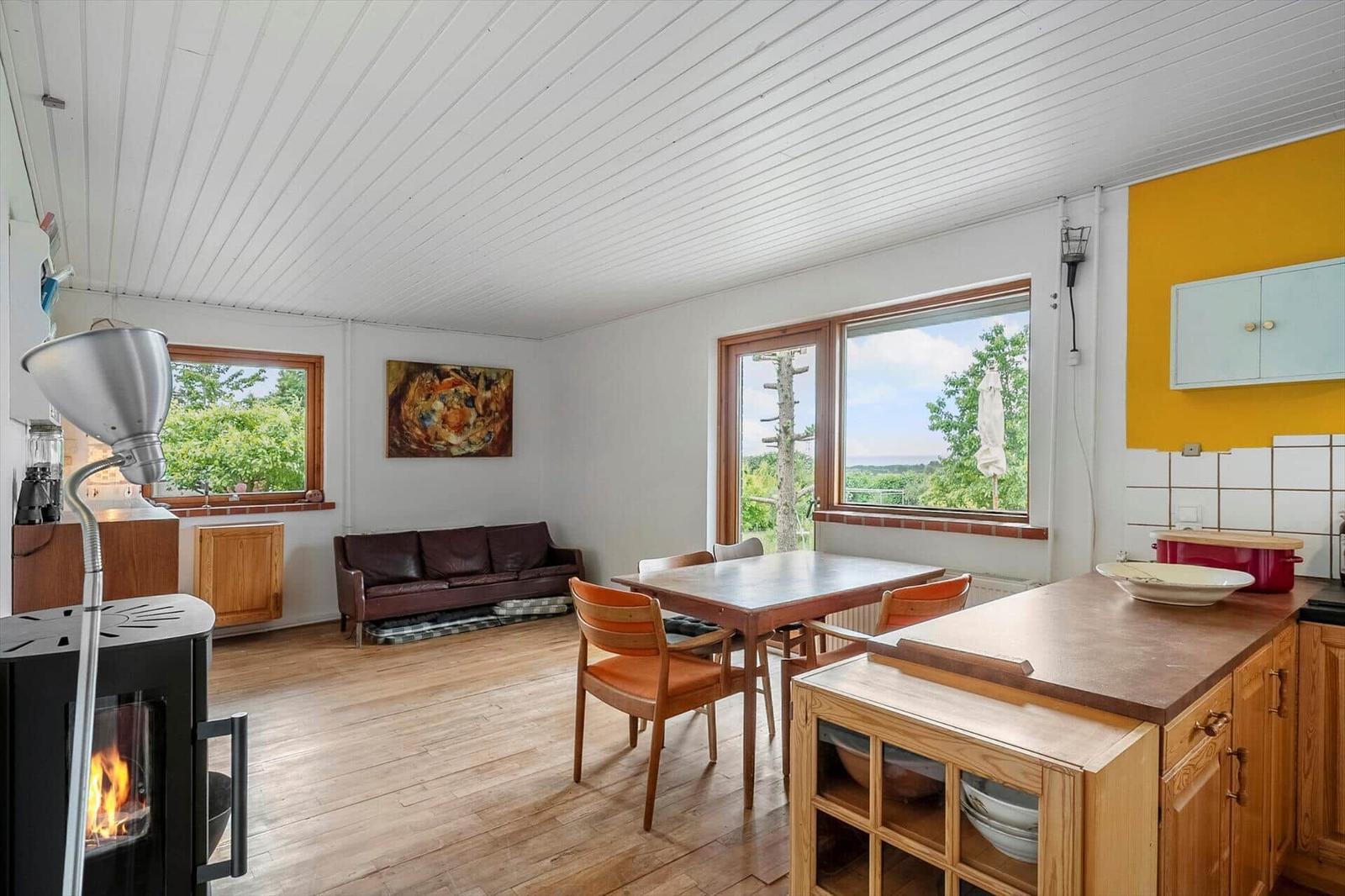 Wohnküche mit Esstisch, Sofa und Kaminofen. Blick auf grüne Landschaft.