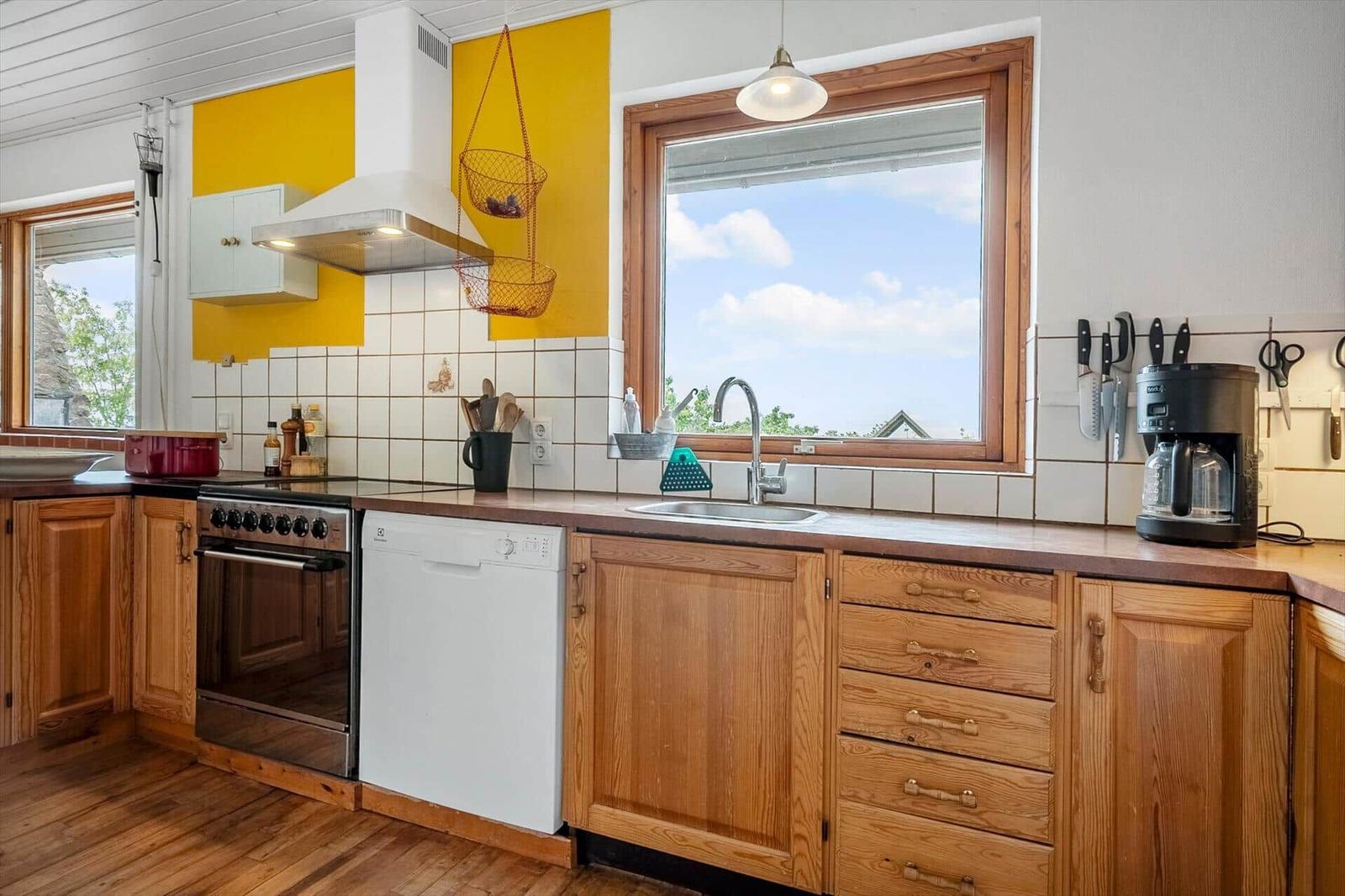 Küche mit Holzschränken, Spüle und Fenster. Gelbe Wand und Edelstahlherd.