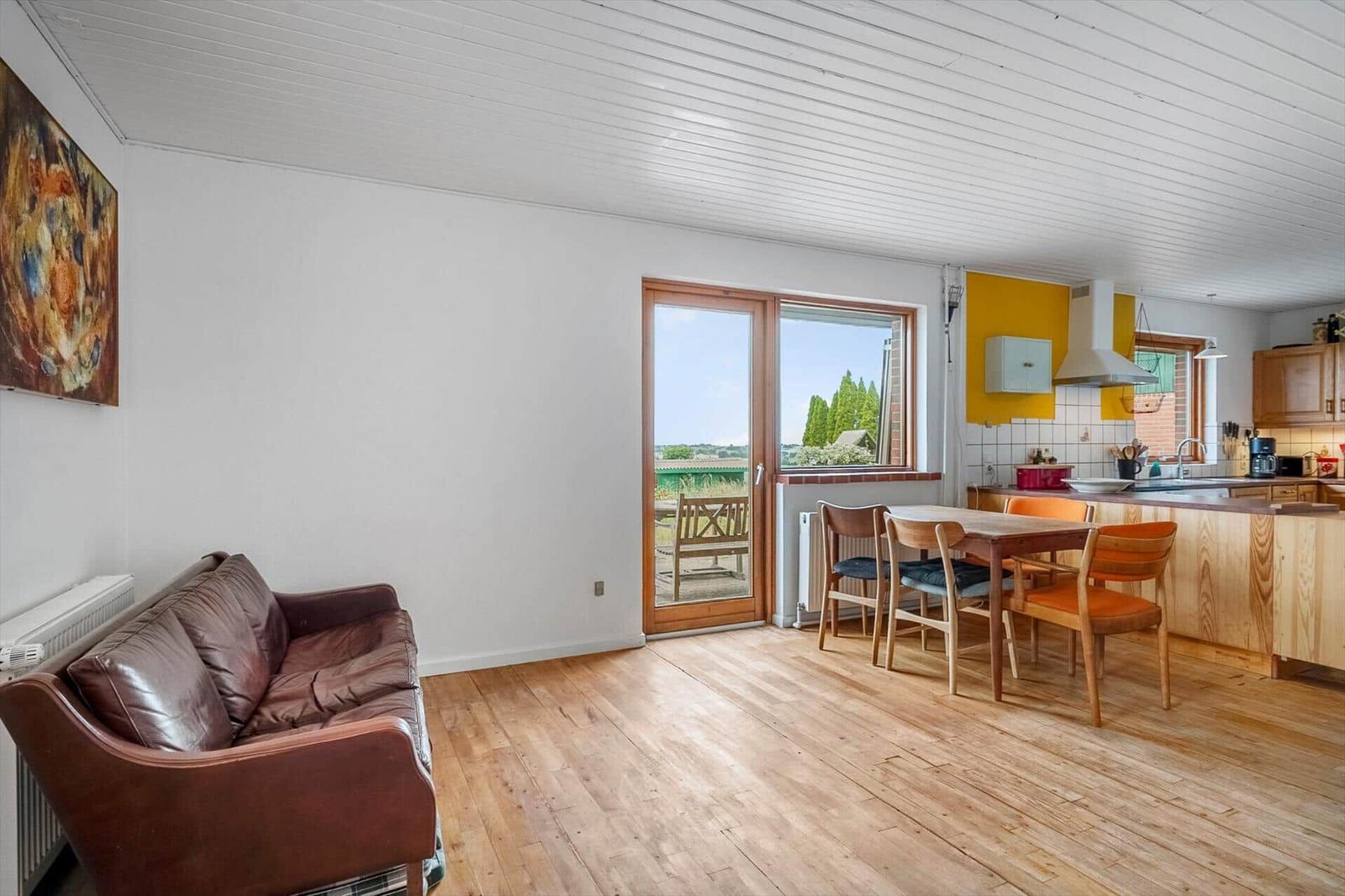 Wohn- und Essbereich mit Holzboden, Sofa und Küchenzeile. Durchgang zur Terrasse.