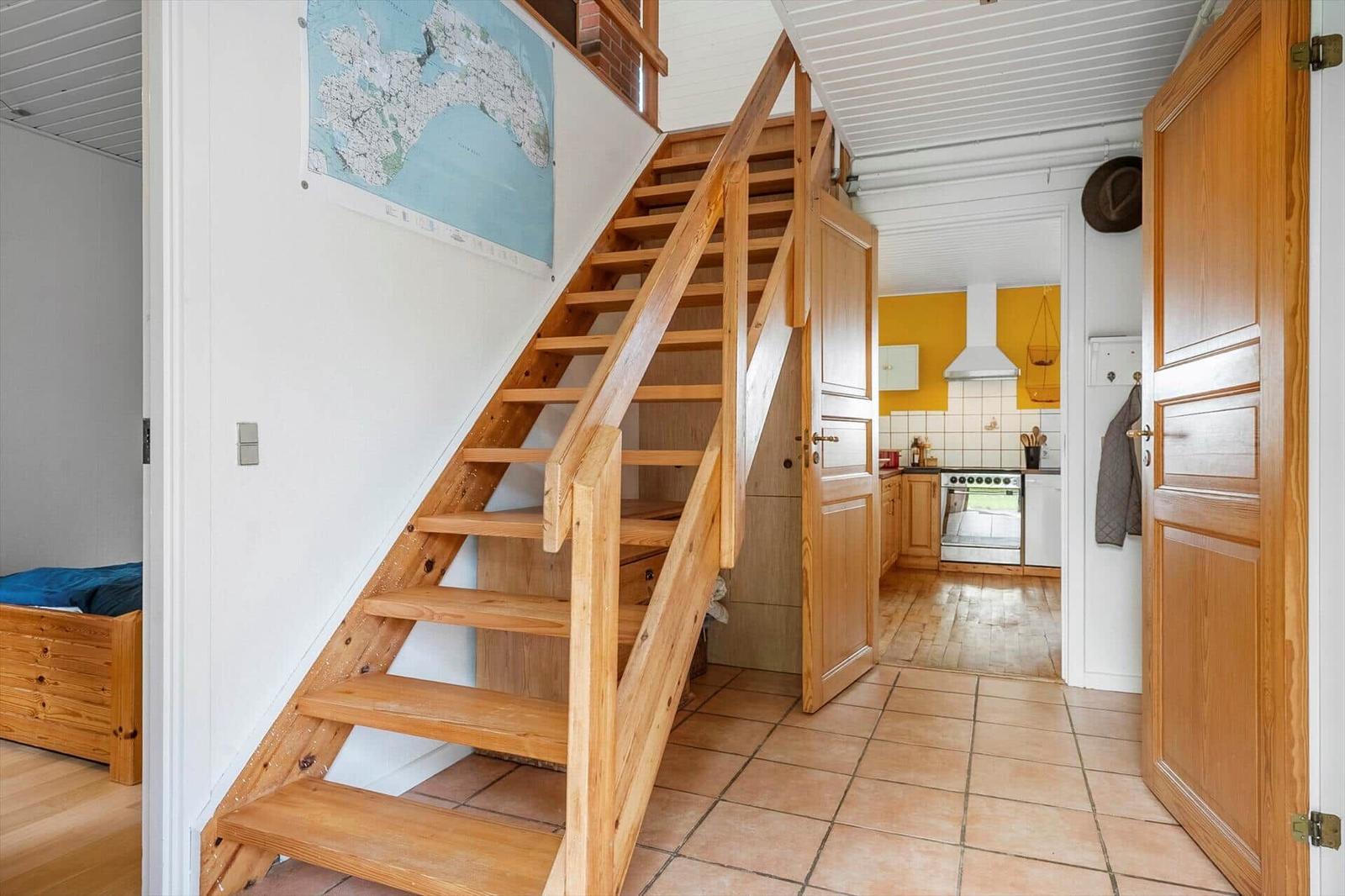 Holztreppe führt zur oberen Etage. Küche mit gelben Wänden und weißen Schränken.
