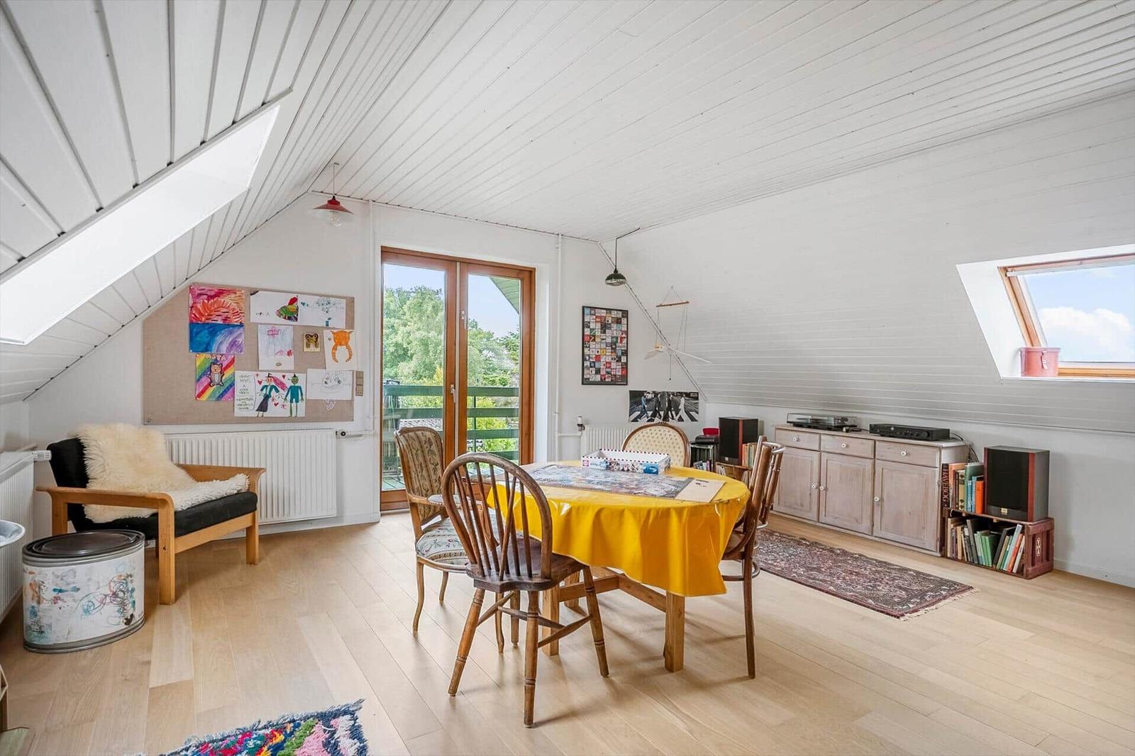 Dachgeschosszimmer mit Esstisch, Sitzgelegenheit und Fenstern. Holzboden und weiße Wände.