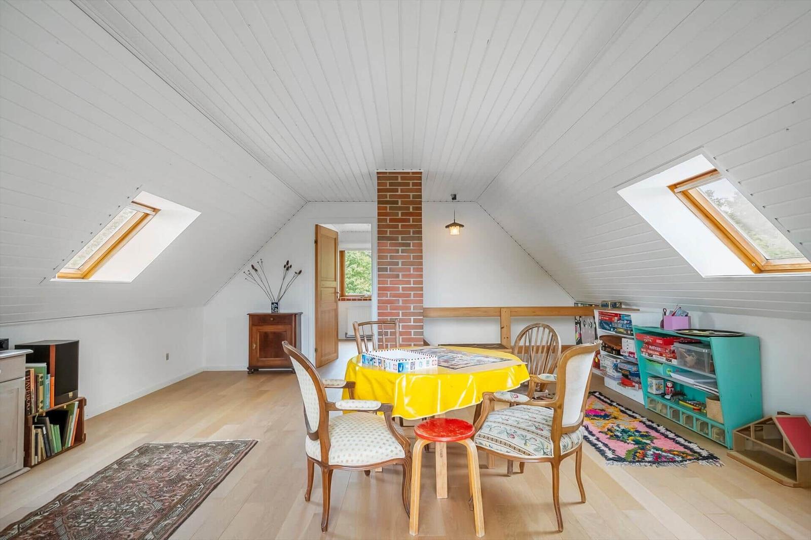 Dachgeschosszimmer mit Tisch, Stühlen und Dachfenstern. Holzboden und Bücherregale.