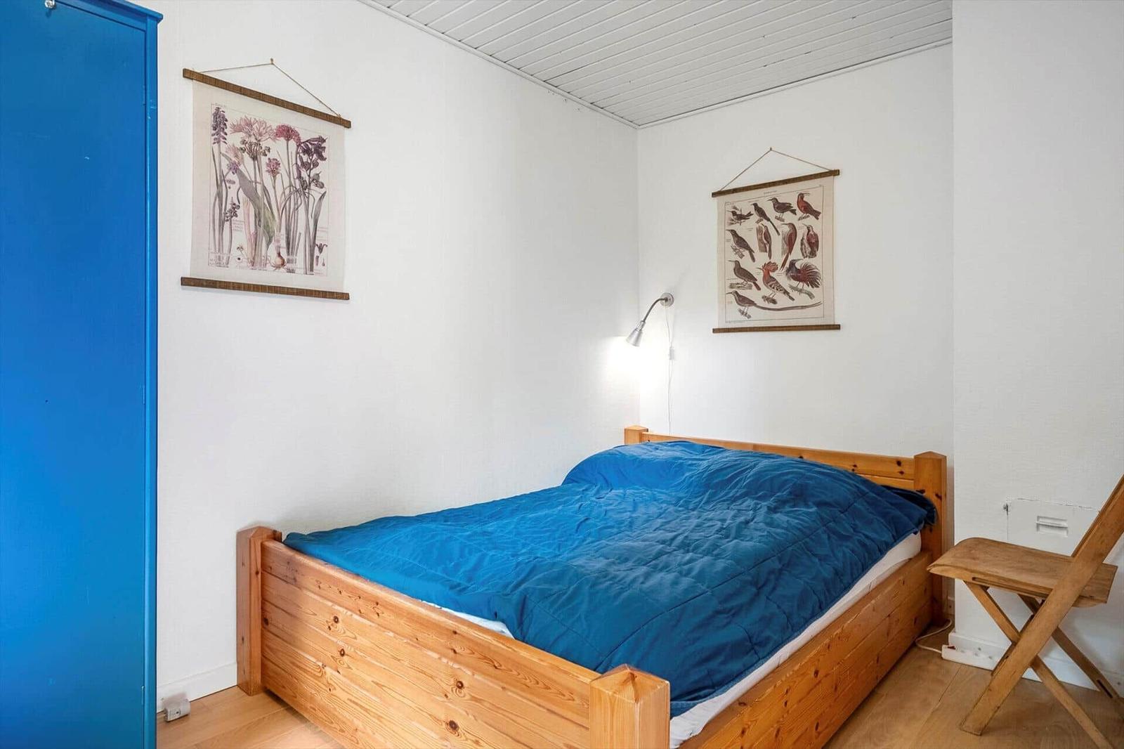 Ein Schlafzimmer mit Holzbett, blauer Bettwäsche, Wandbildern und einem blauen Schrank.