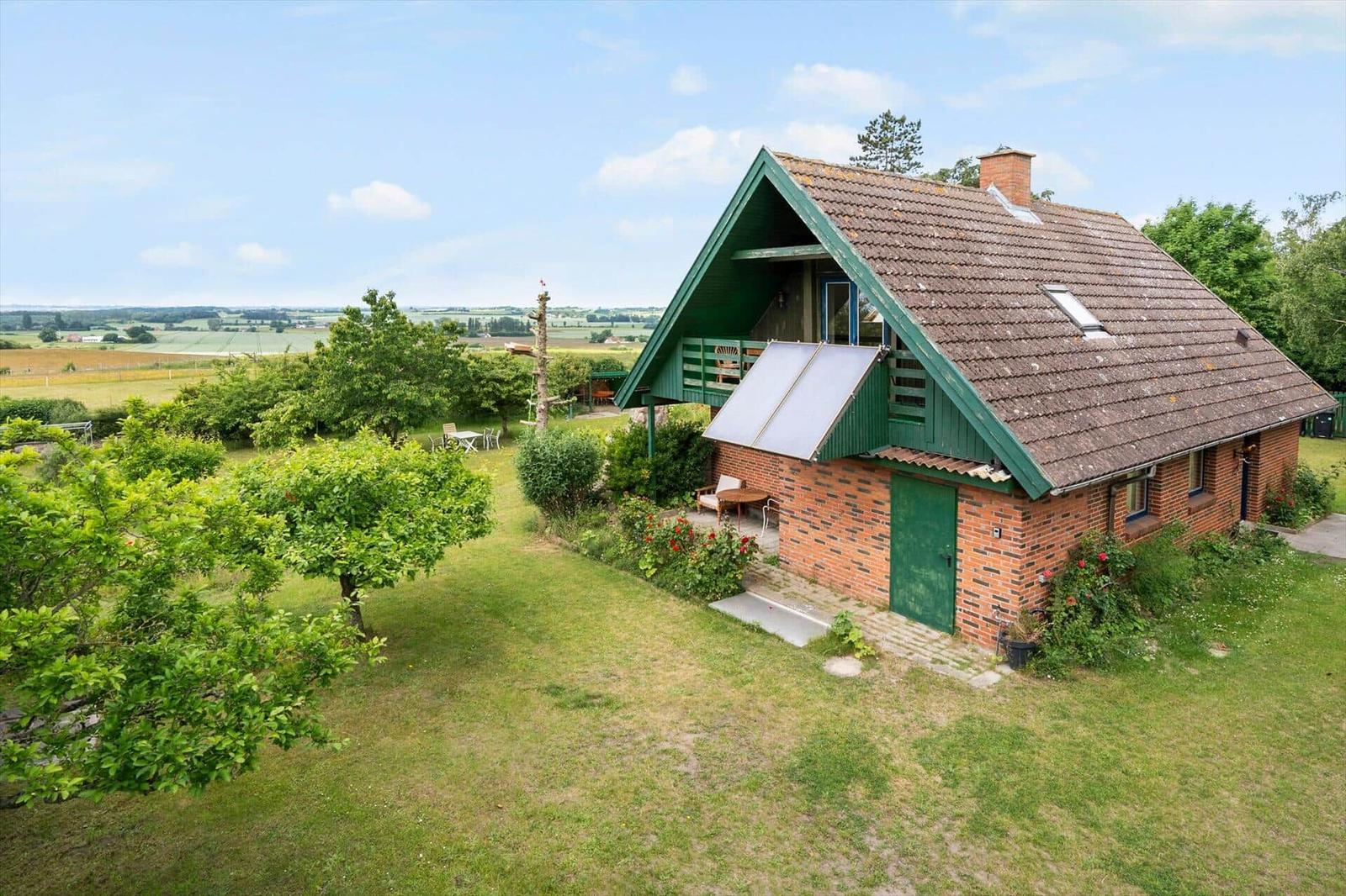 Ein Haus mit grünem Dach und Backsteinfassade auf einer grünen Wiese.