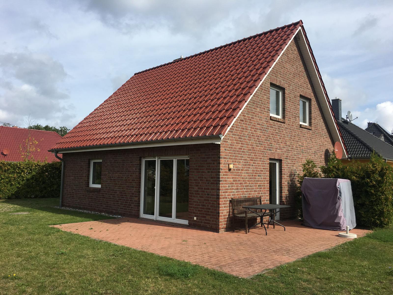 Ein Haus mit rotem Dach und Backsteinfassade. Außenbereich mit Tisch, Stühlen und Grill.