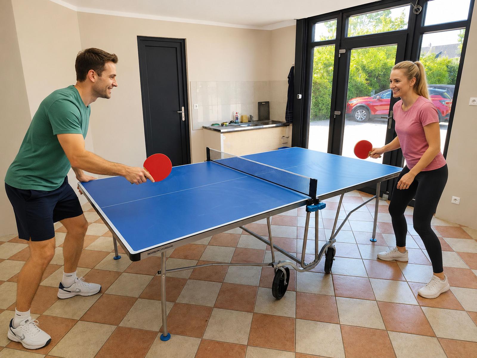 Ein Paar spielt Tischtennis in einem Raum mit Fliesenboden und großen Fenstern.