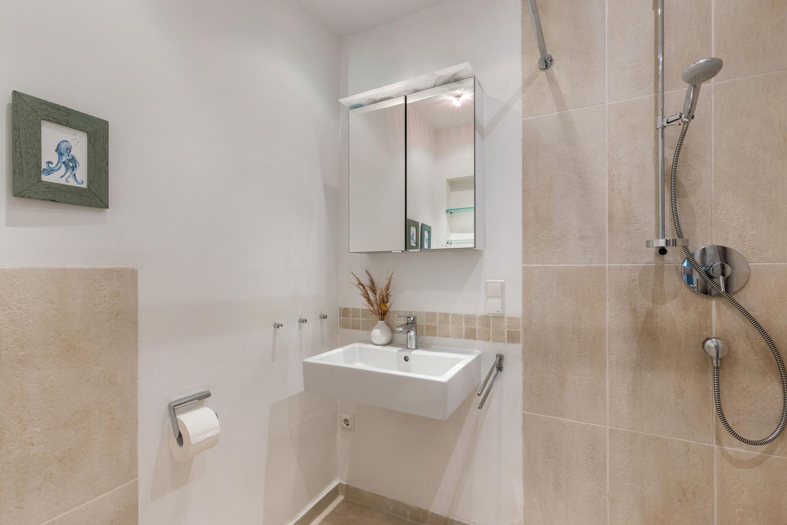 Badezimmer mit Dusche, Waschbecken und Spiegelschrank. Wandbild mit Tintenfisch.