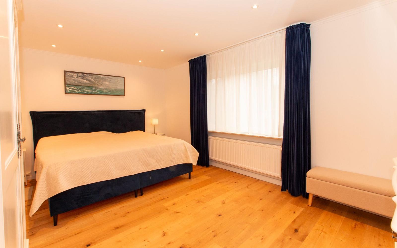 Schlafzimmer mit Doppelbett, Holzboden und Fenster mit Vorhängen.