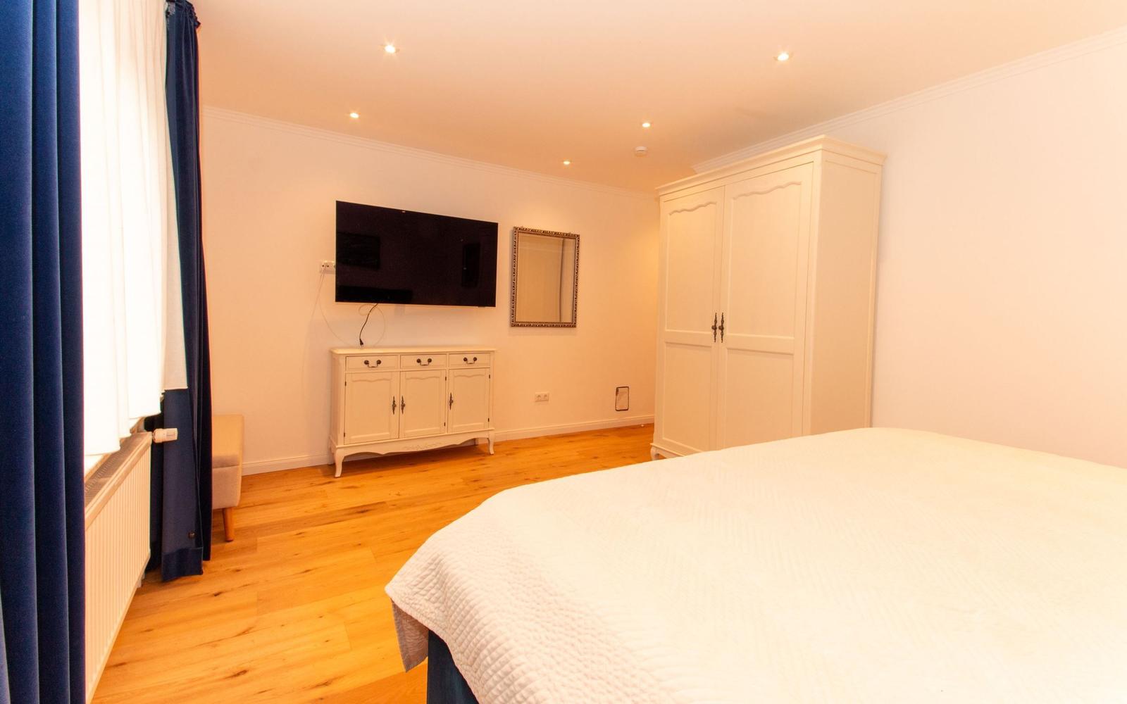 Schlafzimmer mit Bett, Kleiderschrank, TV und Holzboden.
