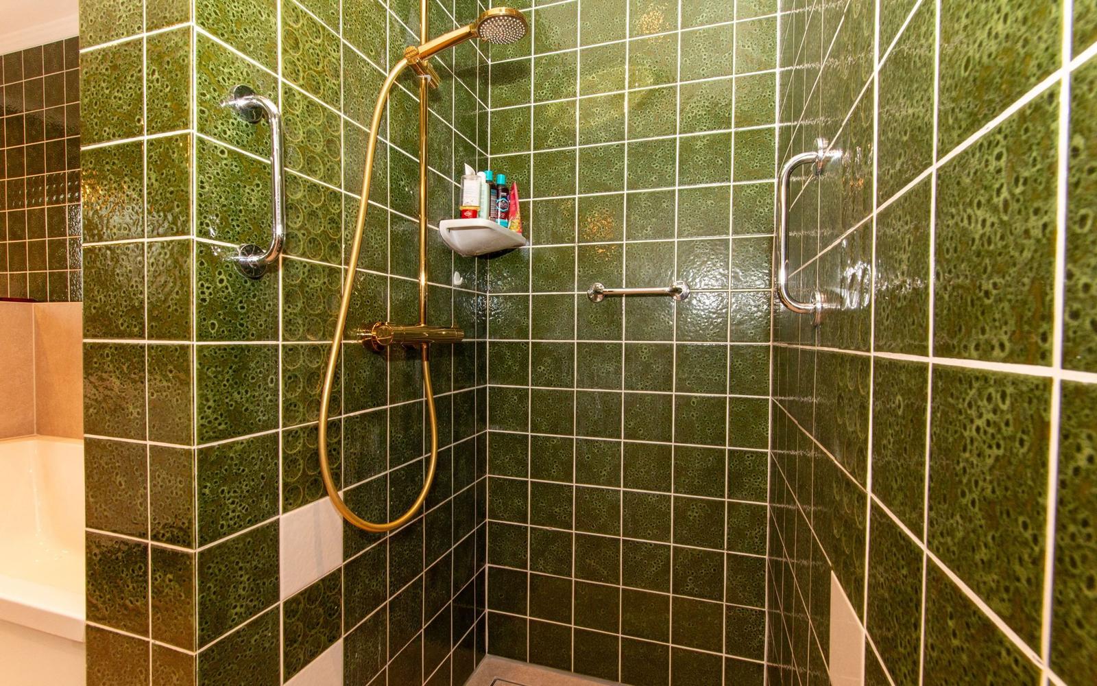 Dusche mit grünen Fliesen und goldfarbenem Duschsystem
