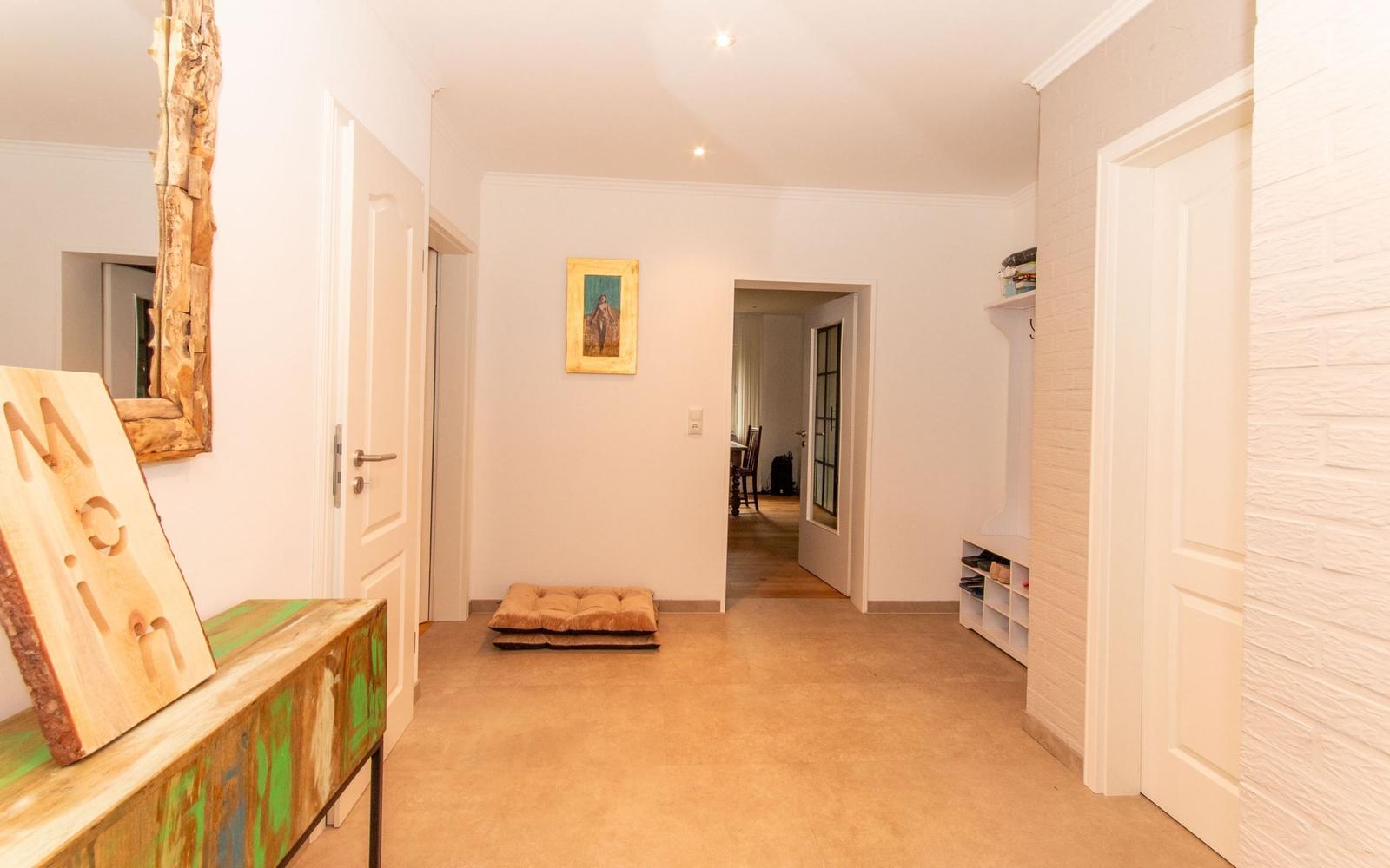 Flur mit Holzboden, Wandbild und Schuhschrank. Links Spiegel und Tisch mit Holzschild.