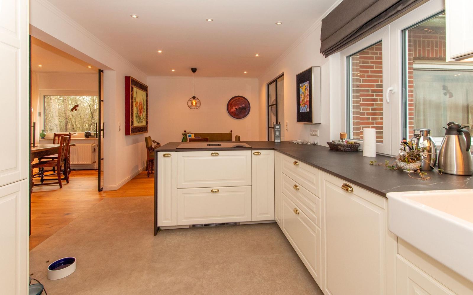 Küche mit weißen Schränken und dunklem Arbeitsplatz. Blick in Esszimmer mit Holzboden.