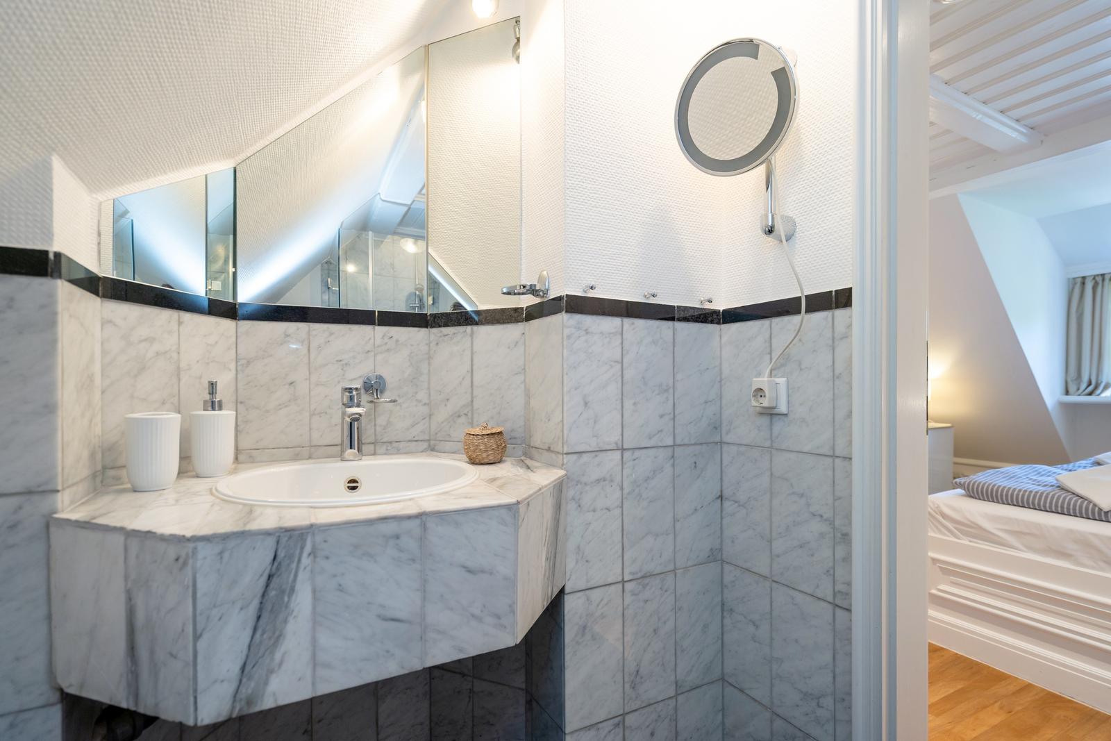 Badezimmer mit Marmorarbeitsplatte, Spiegel und Dusche. Blick in das Schlafzimmer.