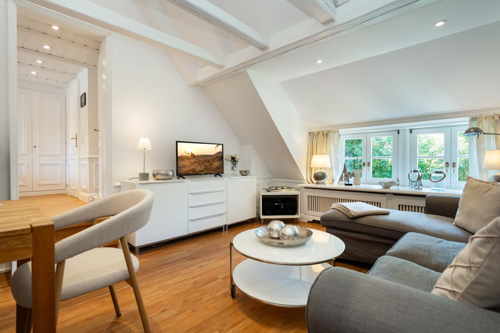Wohnbereich mit Sofa, TV und Fenster mit Blick auf Grün.