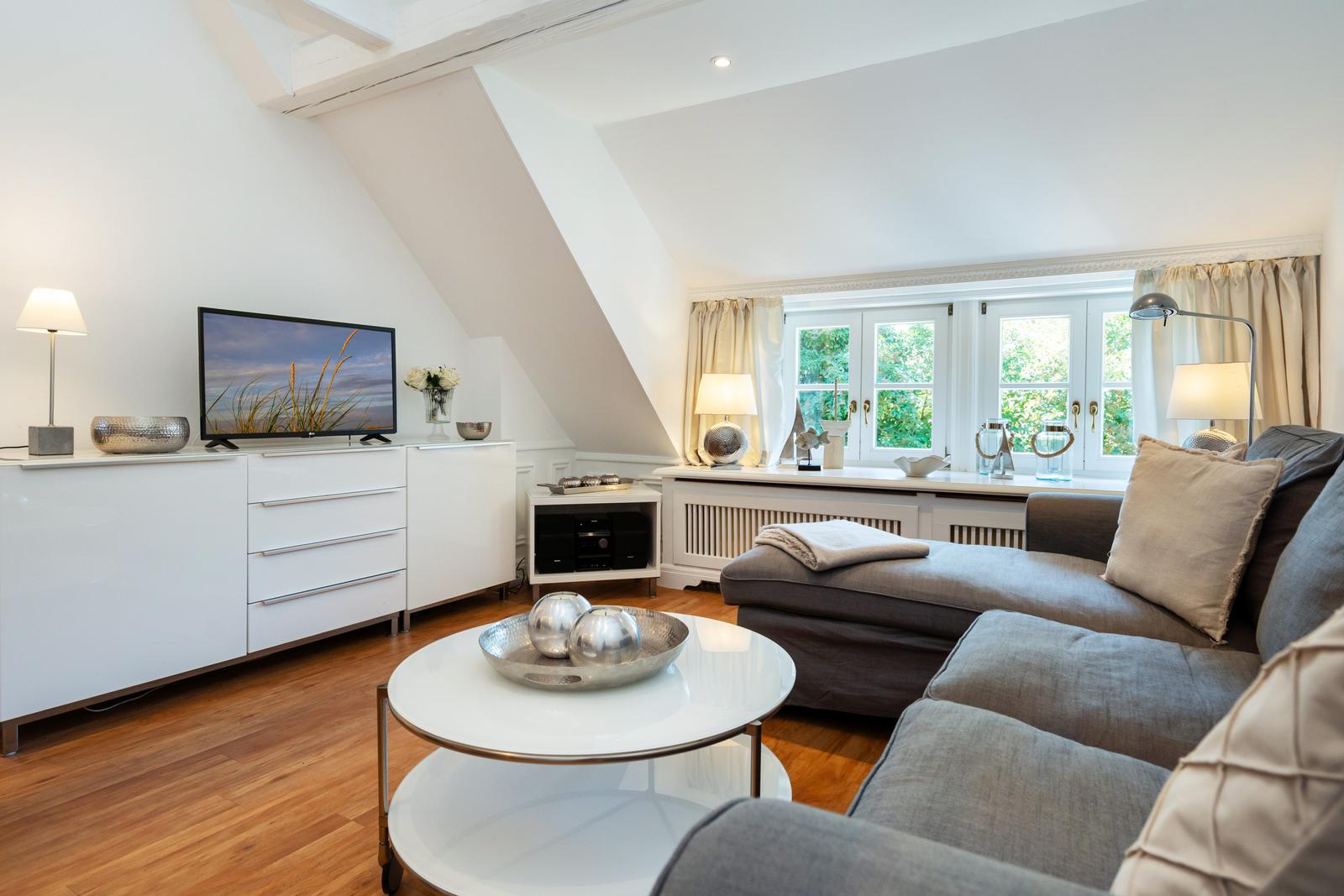 Wohnzimmer mit Sofa, Fernseher und Fenster mit Blick auf Grün.