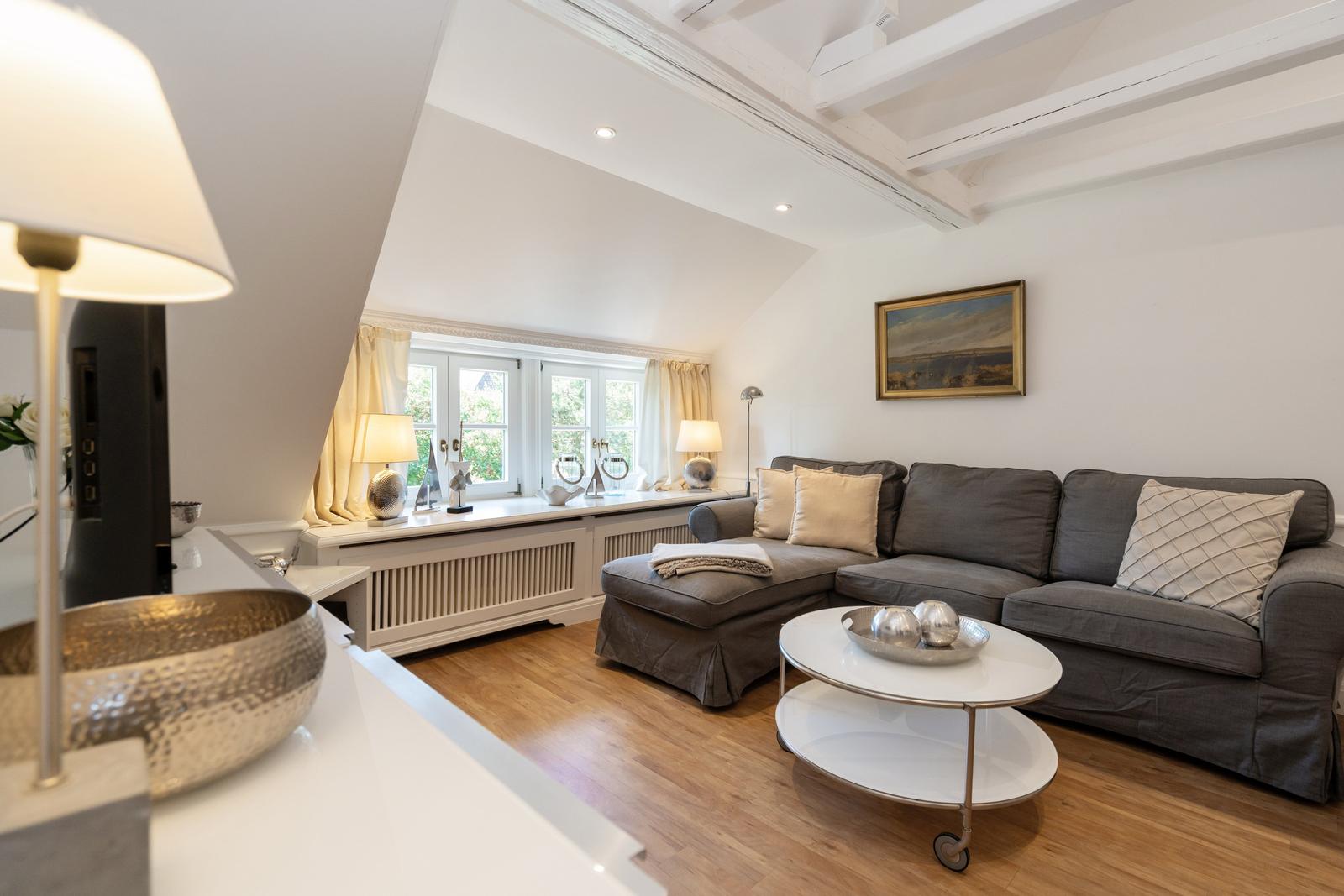 Wohnzimmer mit grauem Sofa, runden Tisch und Fenster mit Blick nach draußen.