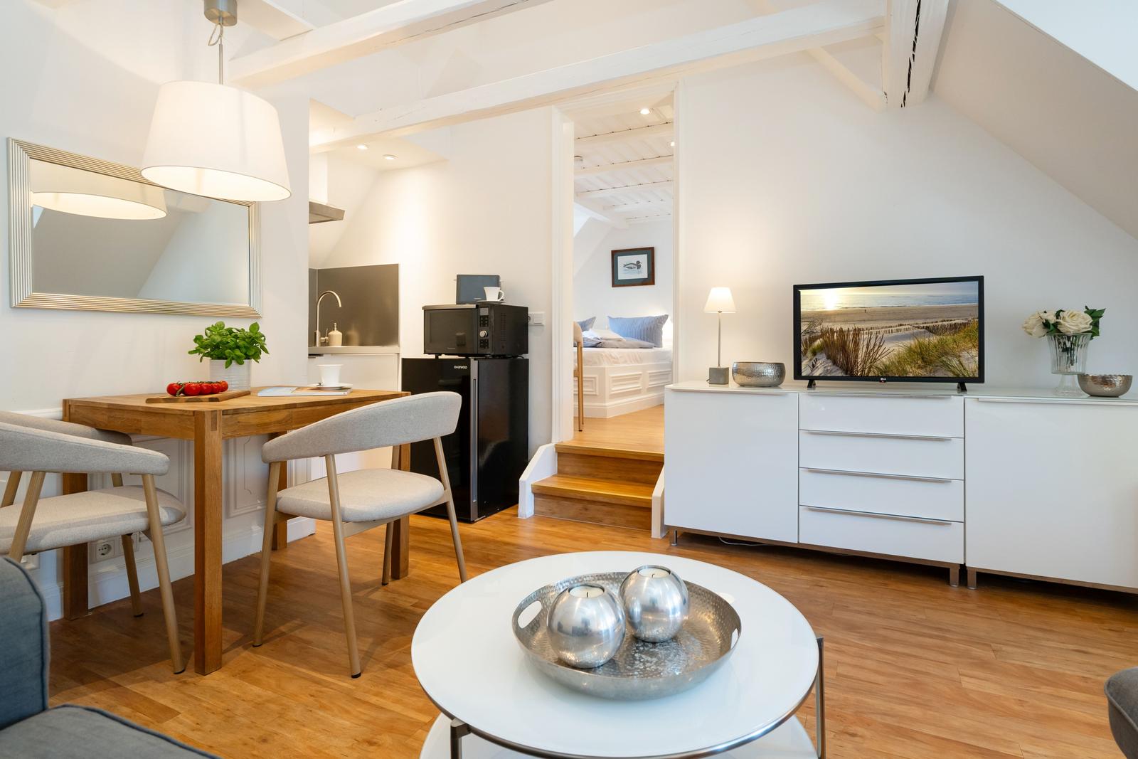 Wohnung mit Essbereich, TV und Schlafzimmer im Hintergrund.