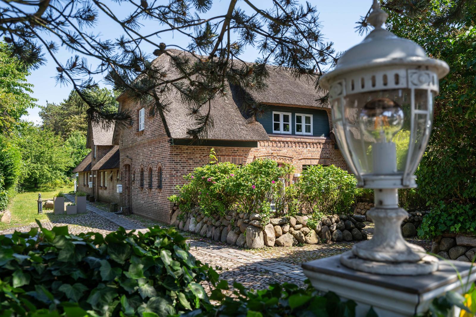 Traditionelles Backsteingebäude mit Strohdach und Steinmauer im Garten