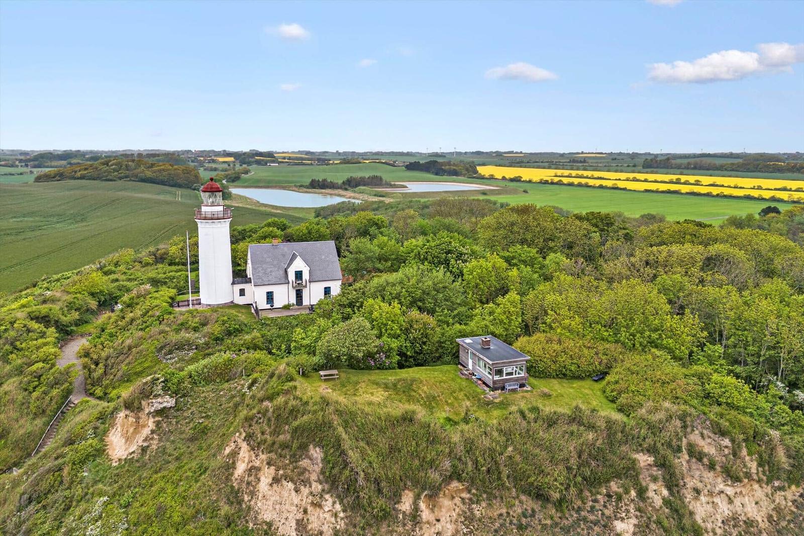 Wohnhaus und Leuchtturm auf grüner Anhöhe mit Blick auf Felder und Wasser.