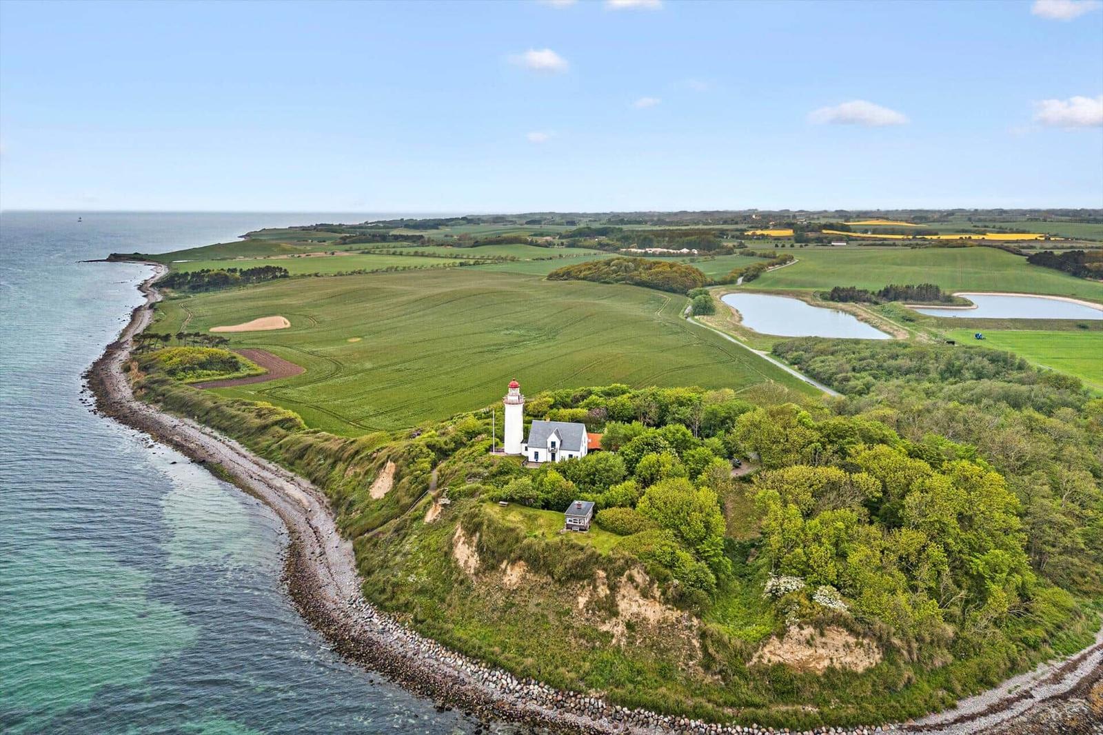 Lichtturm auf grüner Halbinsel mit Feldern und See im Hintergrund