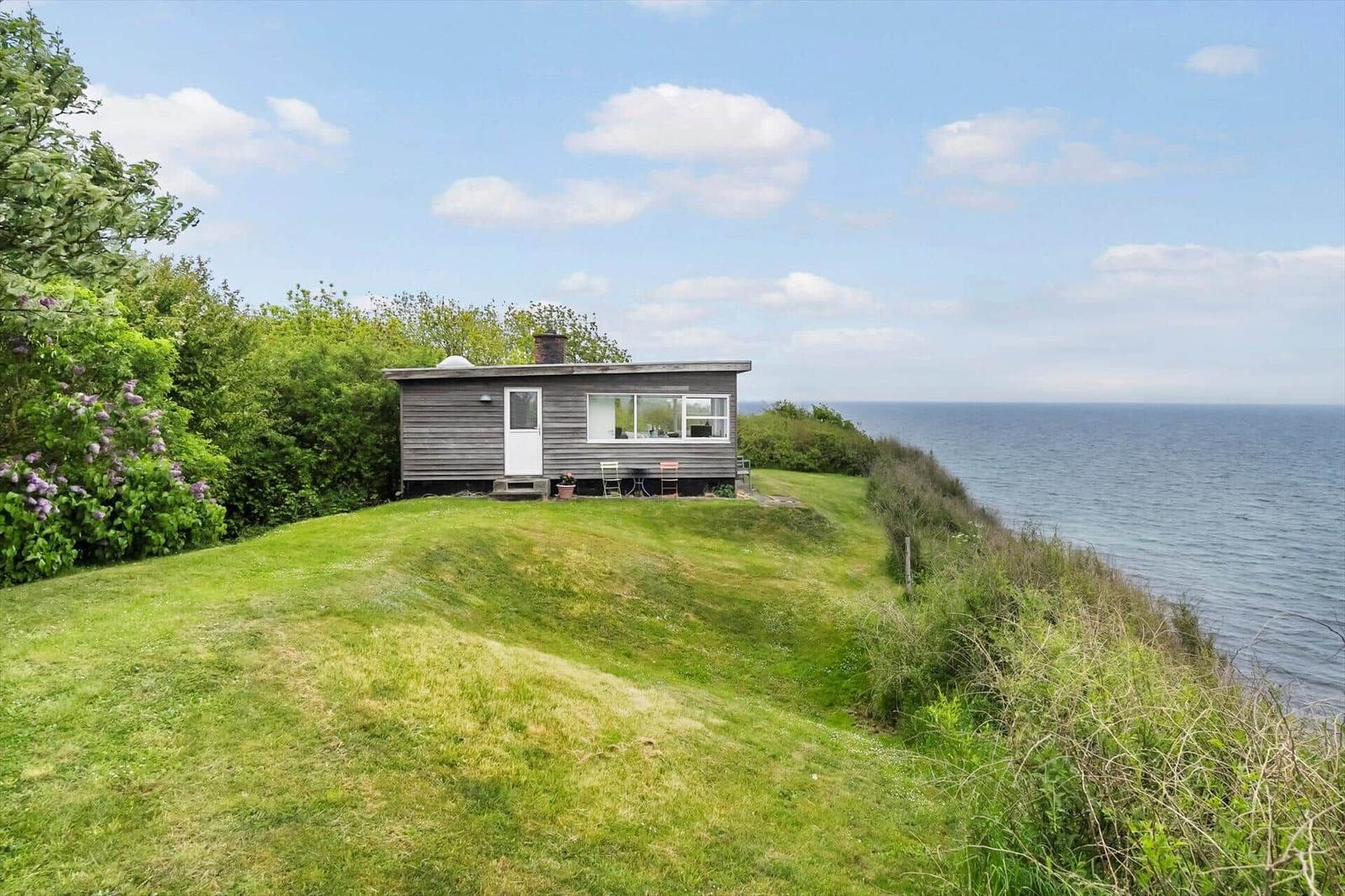 Ein kleines Haus auf einer grünen Anhöhe mit Meerblick und Garten.
