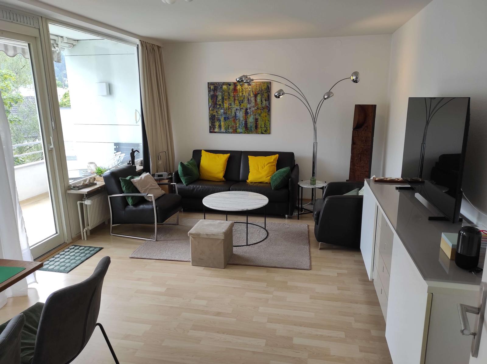 Wohnzimmer mit Sofa, Sitzgelegenheiten und TV. Balkon mit Blick.