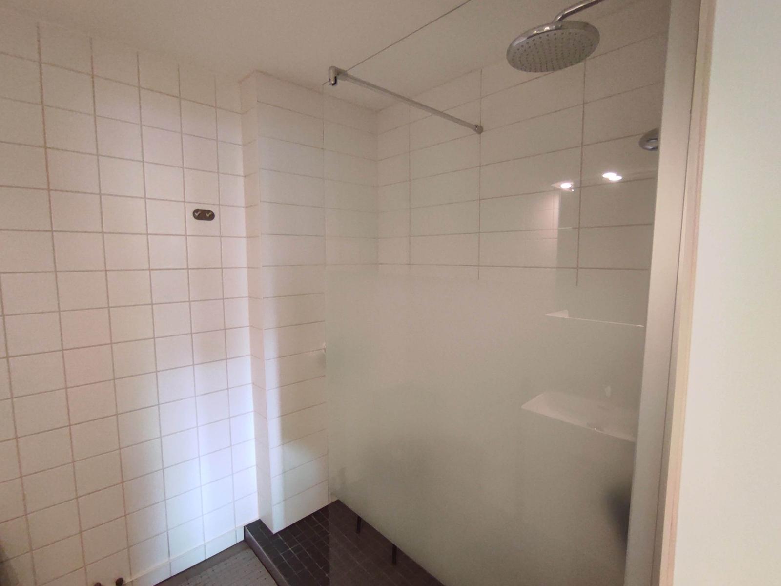 Dusche mit Duschbrause, Glaswand und Fliesenboden.
