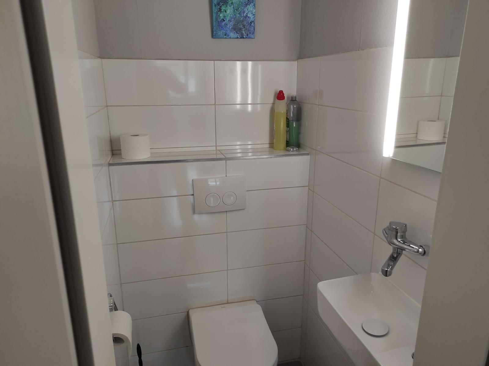 Badezimmer mit Toilette, Waschbecken und Spiegel mit Beleuchtung.