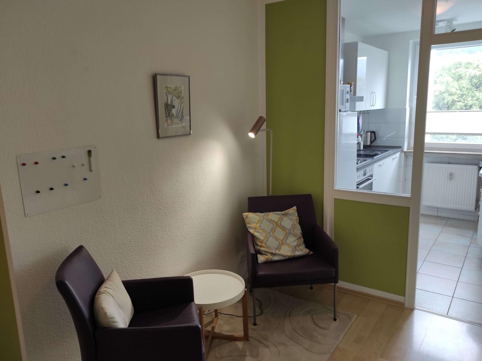 Zwei Sessel, Tisch, Stehlampe und Blick in die Küche.
